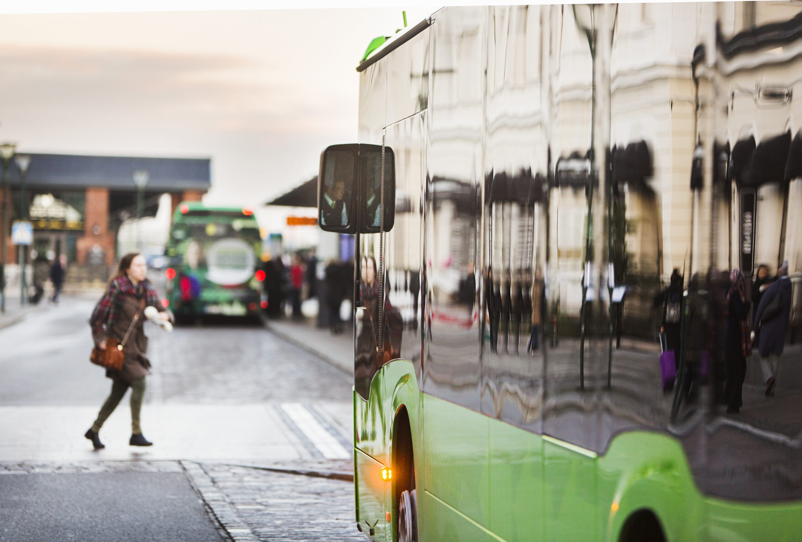 Woman walking by a green bus in the city at dusk